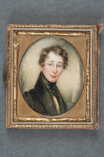 A miniature head and shoulders portrait of a young man. It is oval in shape and is in a gold frame. The young man has short dark hair which is slightly curly. He is wearing a black jacket and a black cravat. A yellow coloured waistcoat with small buttons is just visible under this.
