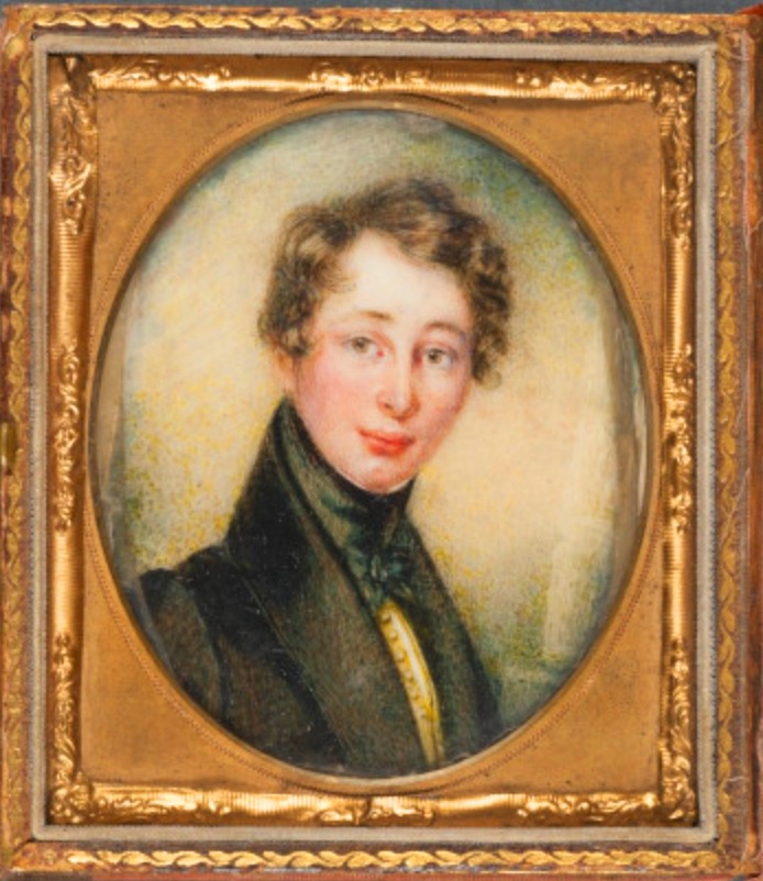A Framed oval quarter-length portrait of young Charles Dickens. IN a golden square frame, he is wearing a black suit jacket with a thick lapel up the back of his neck, a yellow waistcoast and green velvet thick necktie. He is clean shaven with a rosy complexion and medium length side parted wavy brown hair. 