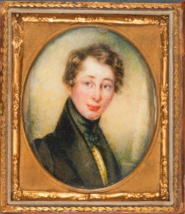 A Framed oval quarter-length portrait of young Charles Dickens. IN a golden square frame, he is wearing a black suit jacket with a thick lapel up the back of his neck, a yellow waistcoast and green velvet thick necktie. He is clean shaven with a rosy complexion and medium length side parted wavy brown hair. 