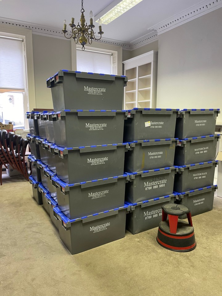 a large number of grey plastic crates are stacked high in a room. 