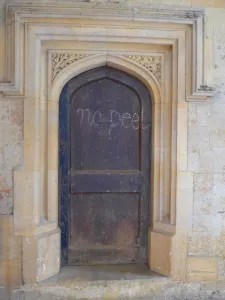 A photograph of a door at Oxford University which has been graffitied. It is a brown wooden door with an ornate stone doorframe carved into the wall. The graffiti on the door reads 'no peel' in simple lower case lettering. 