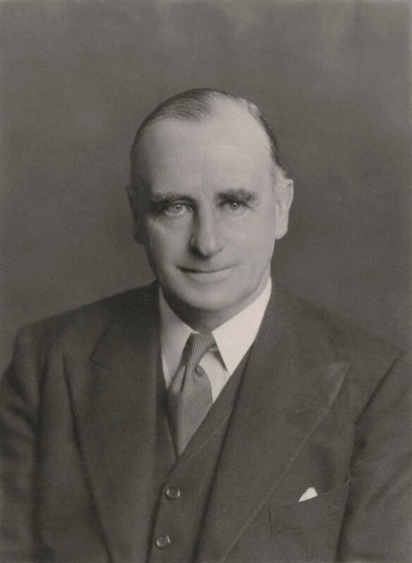 Head and shoulders black and white photograph of a man. He is wearing a three piece suit and a tie. He is balding. 