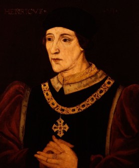 A portrait of a white man wearing robes and a gold chain with a cross. His hands are clasped together.