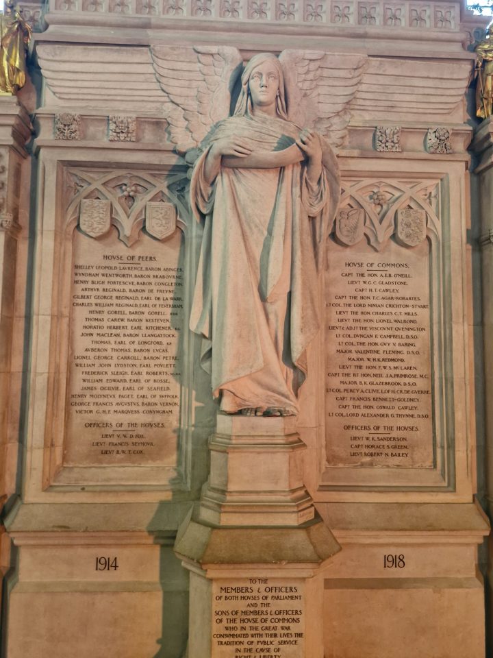 A picture of the central section of the Recording Angel memorial in Westminster Hall. It has a large angel statue in the middle, either side engraved in stone tablets in a large memorial wall are the names of MPs, peers, officers and their sons who lost their lives in the First World War.